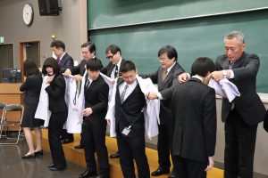 学生に白衣を着せる島田学長ら